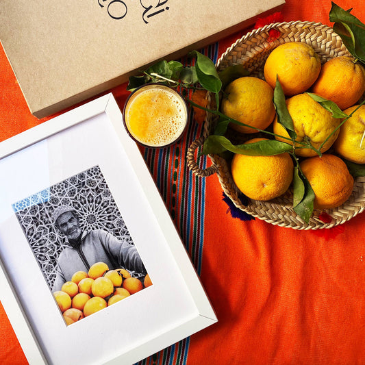 Tableau décoratif en noir et blanc d'un vieux marchand d'oranges très souriant, encadré dans un cadre blanc - Format A4.