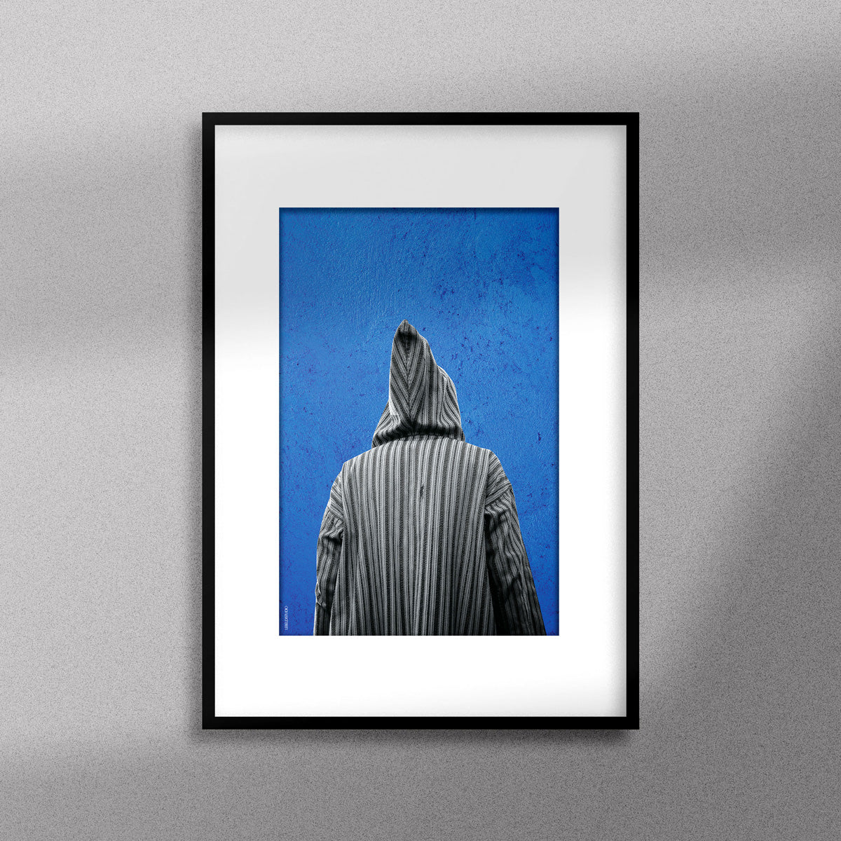 Tableau décoratif représentant un homme portant une djellaba marocaine sur un fond bleu d'un mur peint à la main, encadré dans un cadre noir - Format A3.