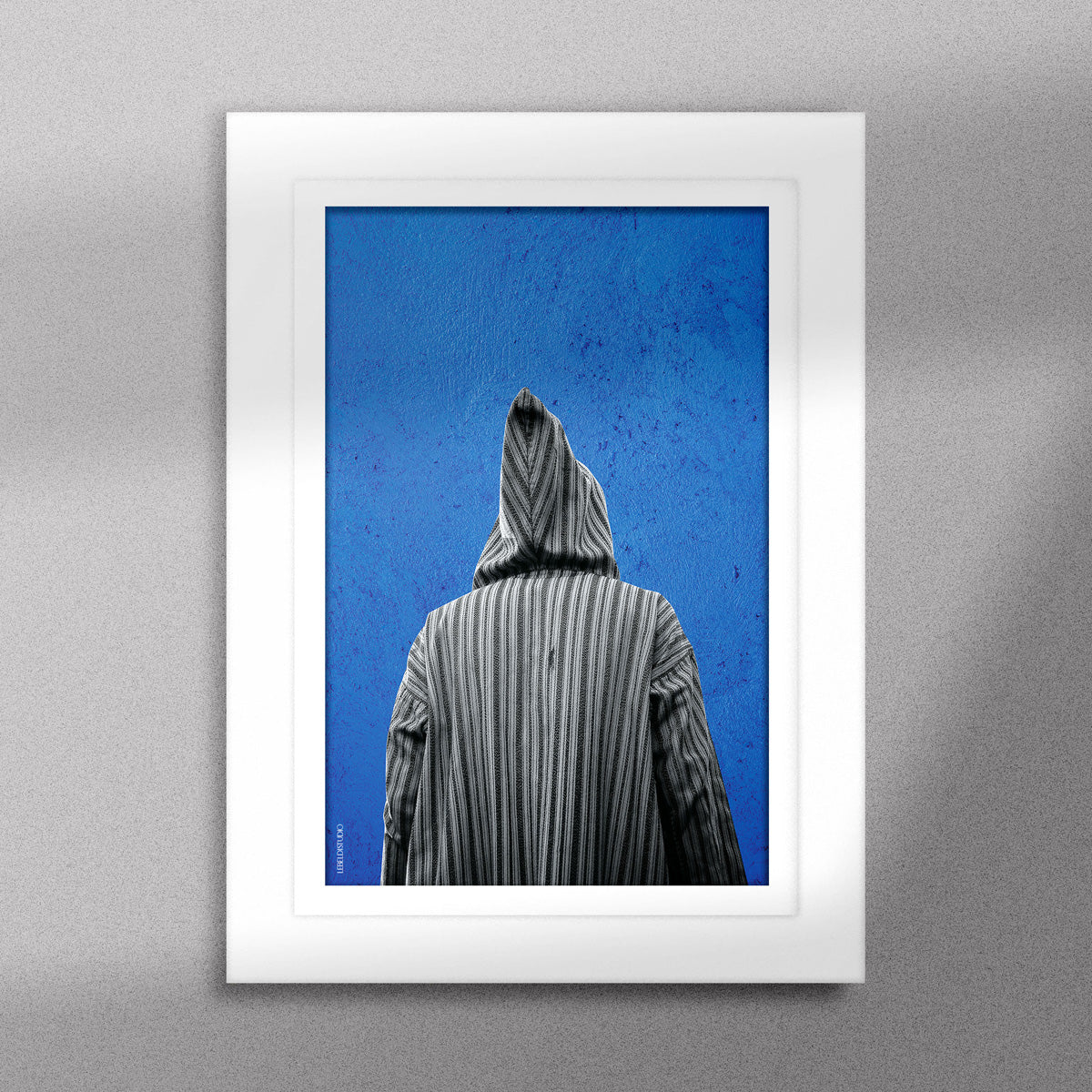 Tableau décoratif représentant un homme portant une djellaba marocaine sur un fond bleu d'un mur peint à la main, encadré dans un cadre blanc - Format A5.