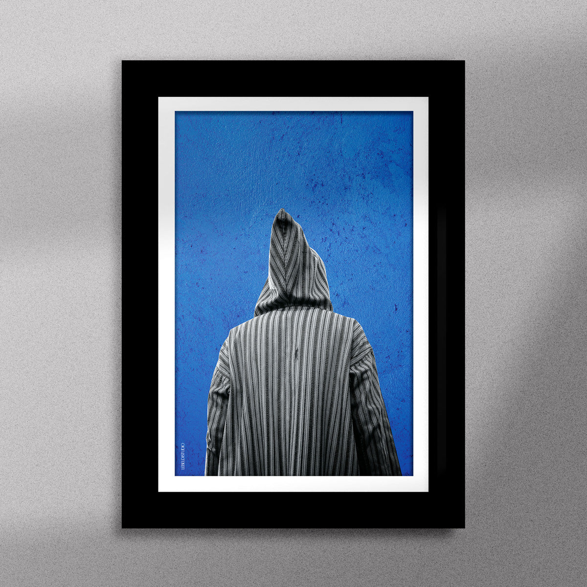 Tableau décoratif représentant un homme portant une djellaba marocaine sur un fond bleu d'un mur peint à la main, encadré dans un cadre noir - Format A5.