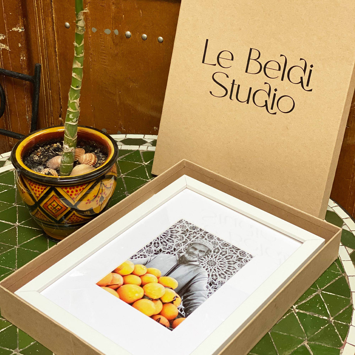 Tableau décoratif en noir et blanc d'un vieux marchand d'oranges très souriant, encadré dans un cadre blanc - Format A4.