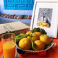 Tableau décoratif en noir et blanc d'un vieux marchand d'oranges très souriant, encadré dans un cadre blanc - Format A4.