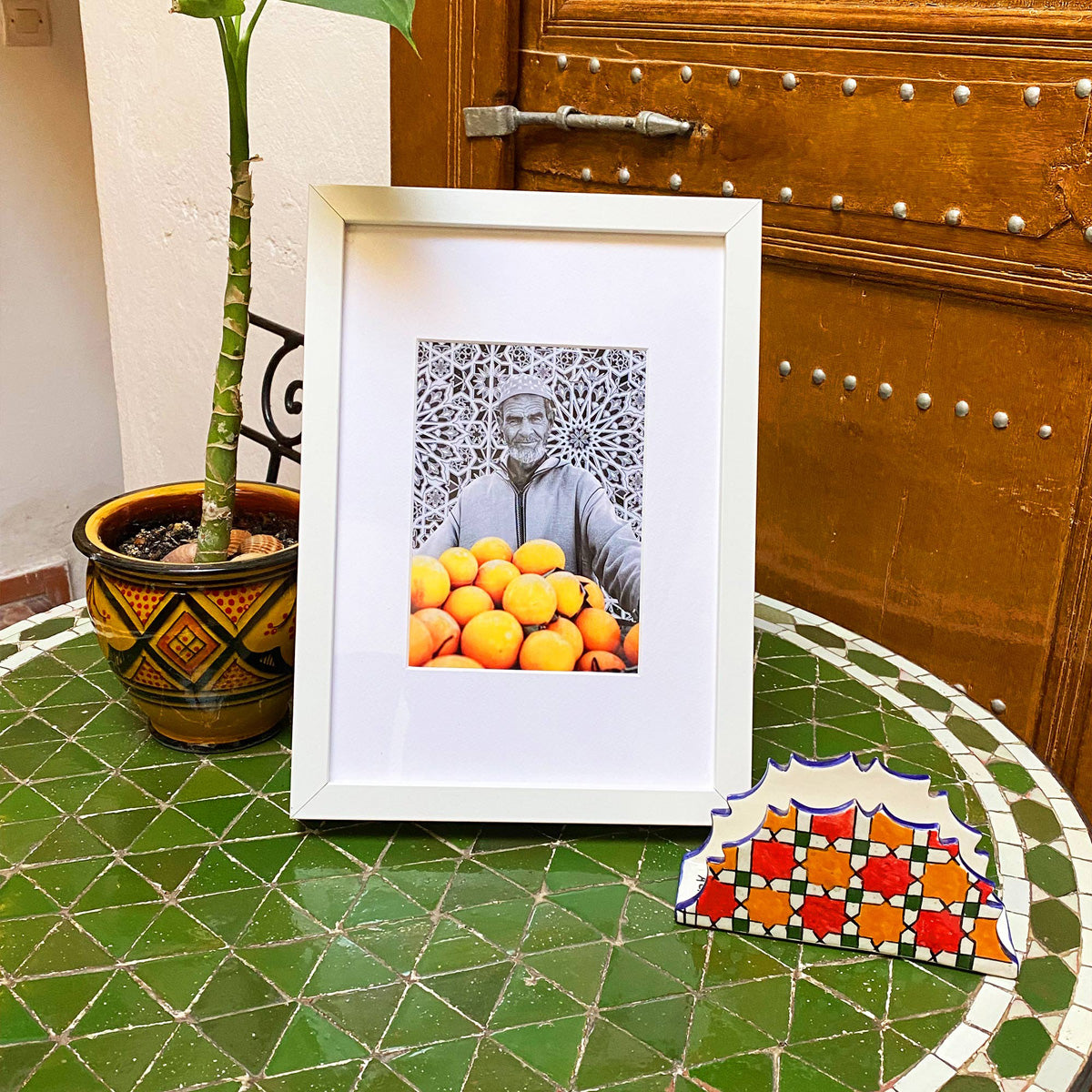Tableau décoratif en noir et blanc d'un vieux marchand d'oranges très souriant, encadré dans un cadre blanc - Format A4.