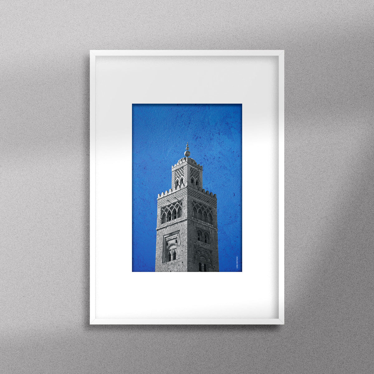Tableau décoratif représentant la Koutoubia de Marrakech sur un fond bleu, encadré dans un cadre blanc - Format A4.