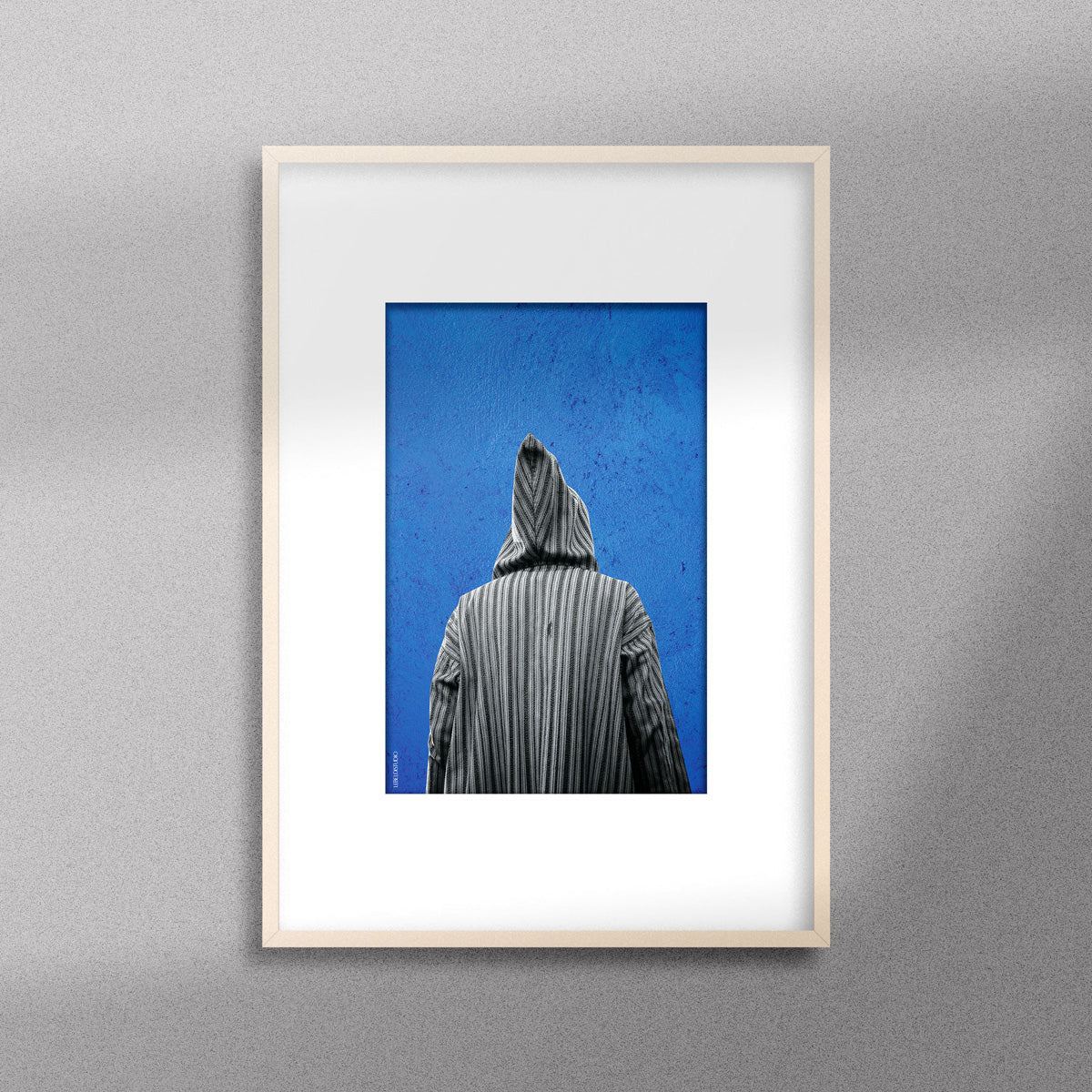 Tableau décoratif représentant un homme portant une djellaba marocaine sur un fond bleu d'un mur peint à la main, encadré dans un cadre en bois - Format A4.