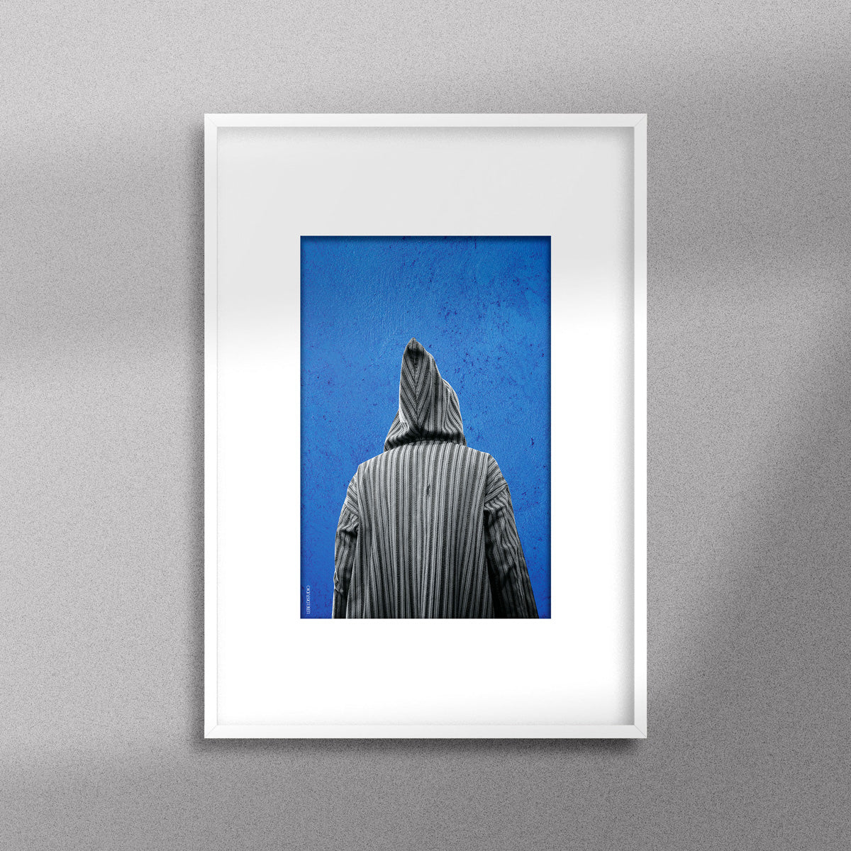 Tableau décoratif représentant un homme portant une djellaba marocaine sur un fond bleu d'un mur peint à la main, encadré dans un cadre blanc - Format A4.