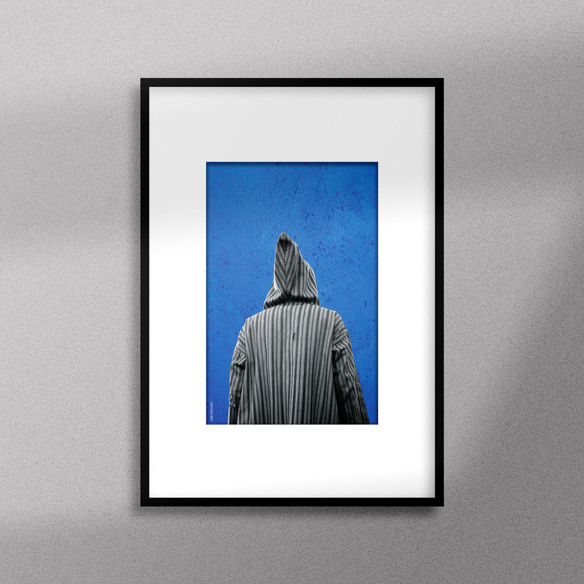 Tableau décoratif représentant un homme portant une djellaba marocaine sur un fond bleu d'un mur peint à la main, encadré dans un cadre noir - Format A4.